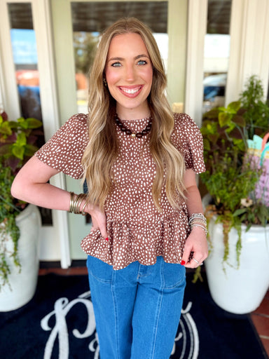 A warm mocha top features an allover ivory spotted print, easy flutter puff sleeves and a feminine peplum hem.
