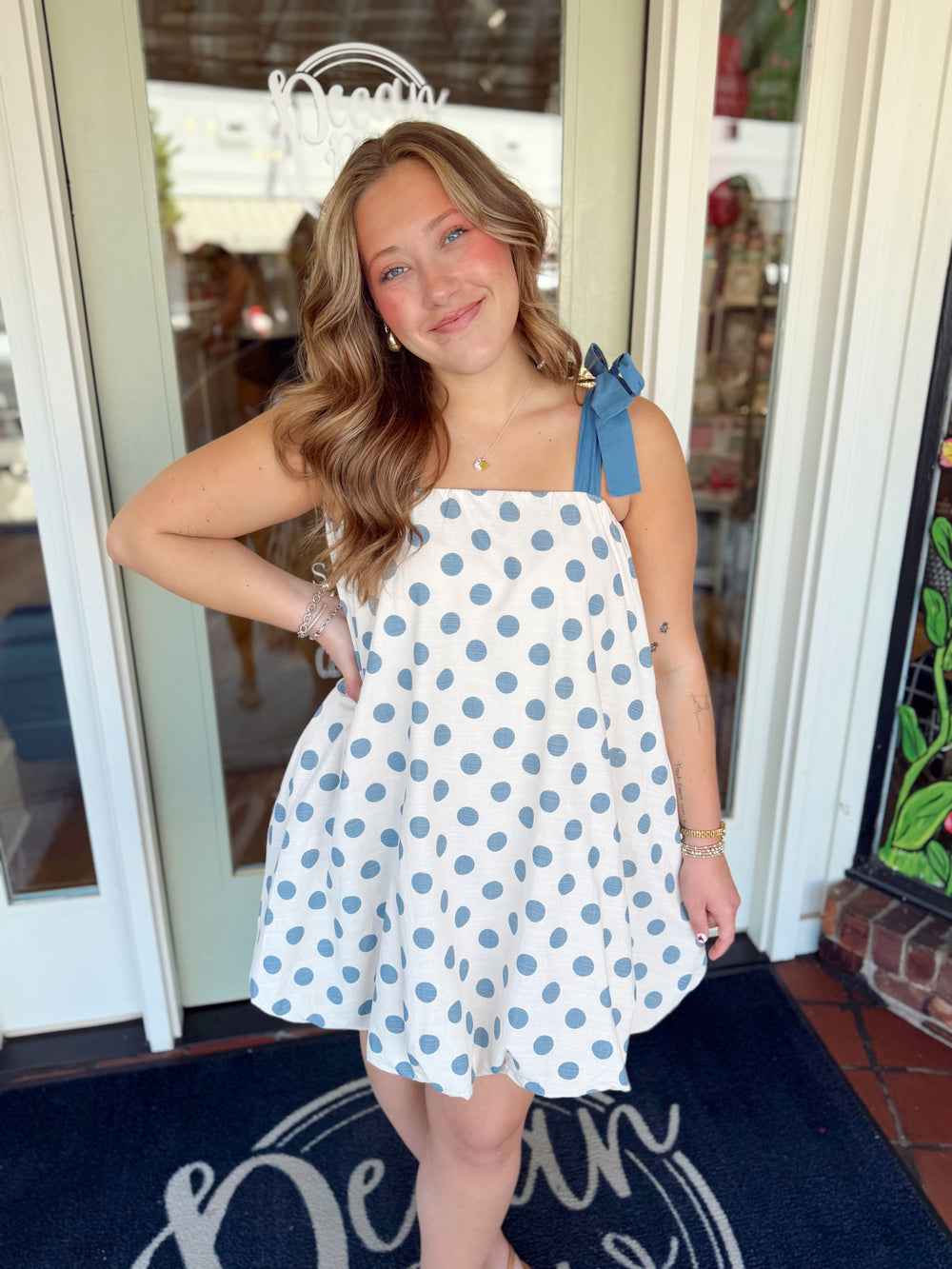 Cream swing mini dress with blue polka dots and adjustable tie shoulder straps.