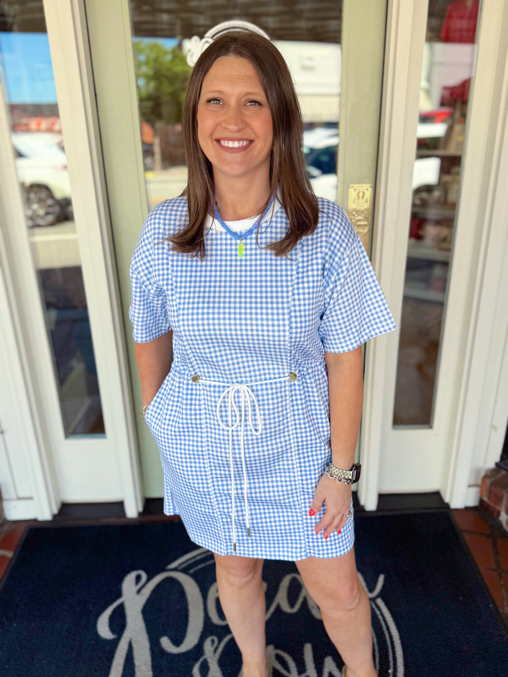 Blue and white gingham short sleeve mini dress with adjustable drawstring waist and relaxed fit.
