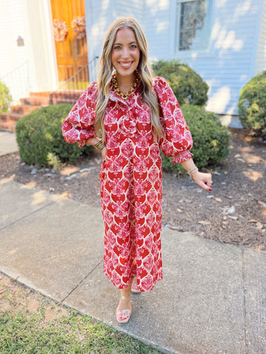 This midi dress features a bold rust and pink statement print with feminine ruffle detailing along the neckline and bodice.