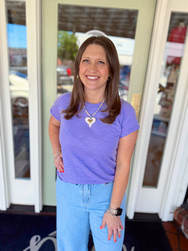 Woman wearing a lavender short sleeve tee paired with light wash denim jeans and a heart pendant necklace.