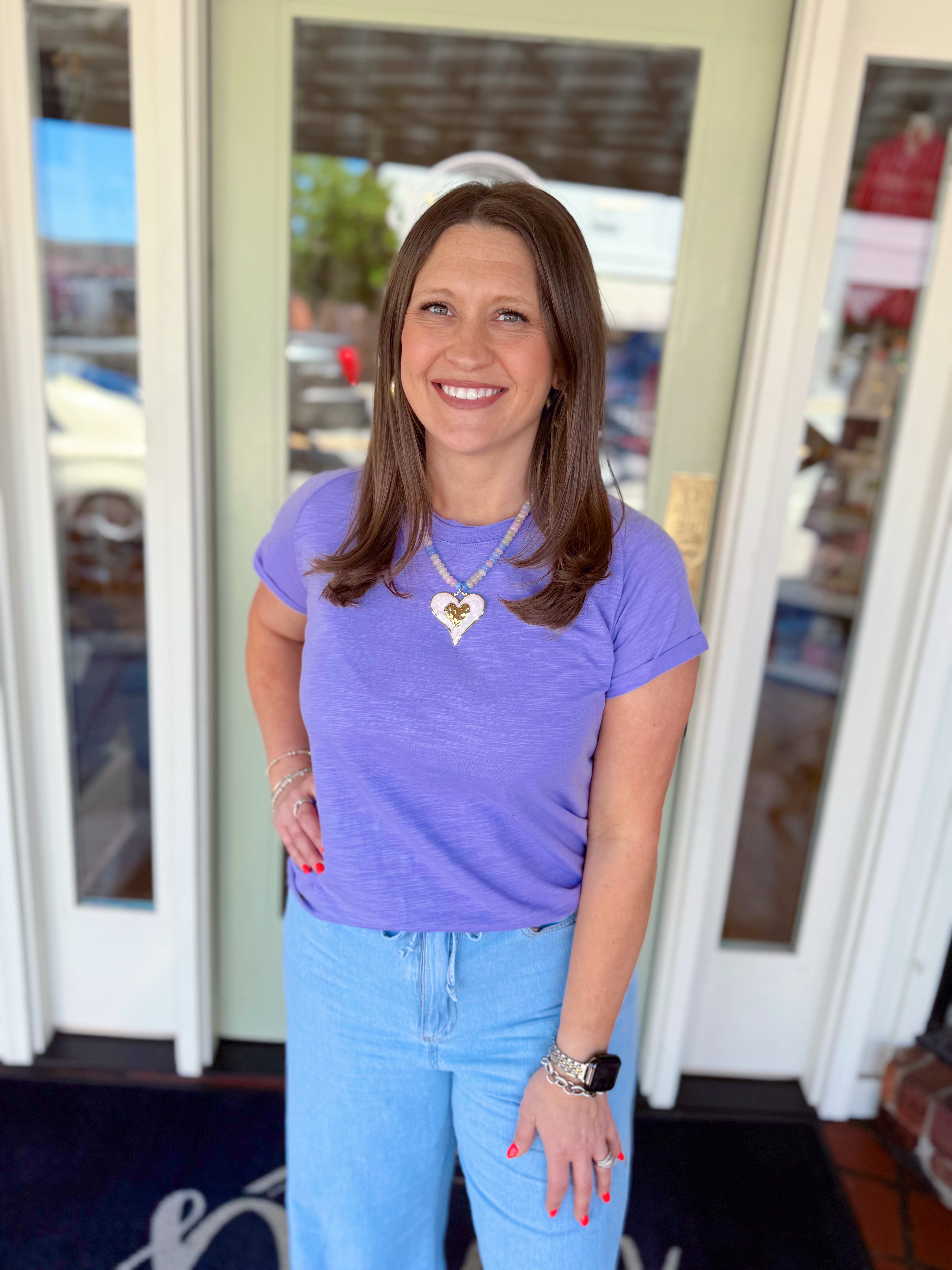 Woman wearing a lavender short sleeve tee paired with light wash denim jeans and a heart pendant necklace.