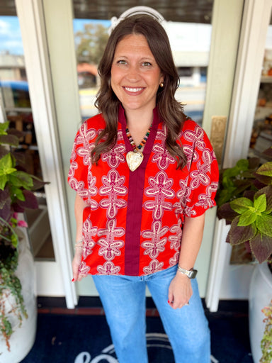  This rust and burgundy printed top features a bold geometric floral design with a contrasting burgundy stand collar and split neckline. 