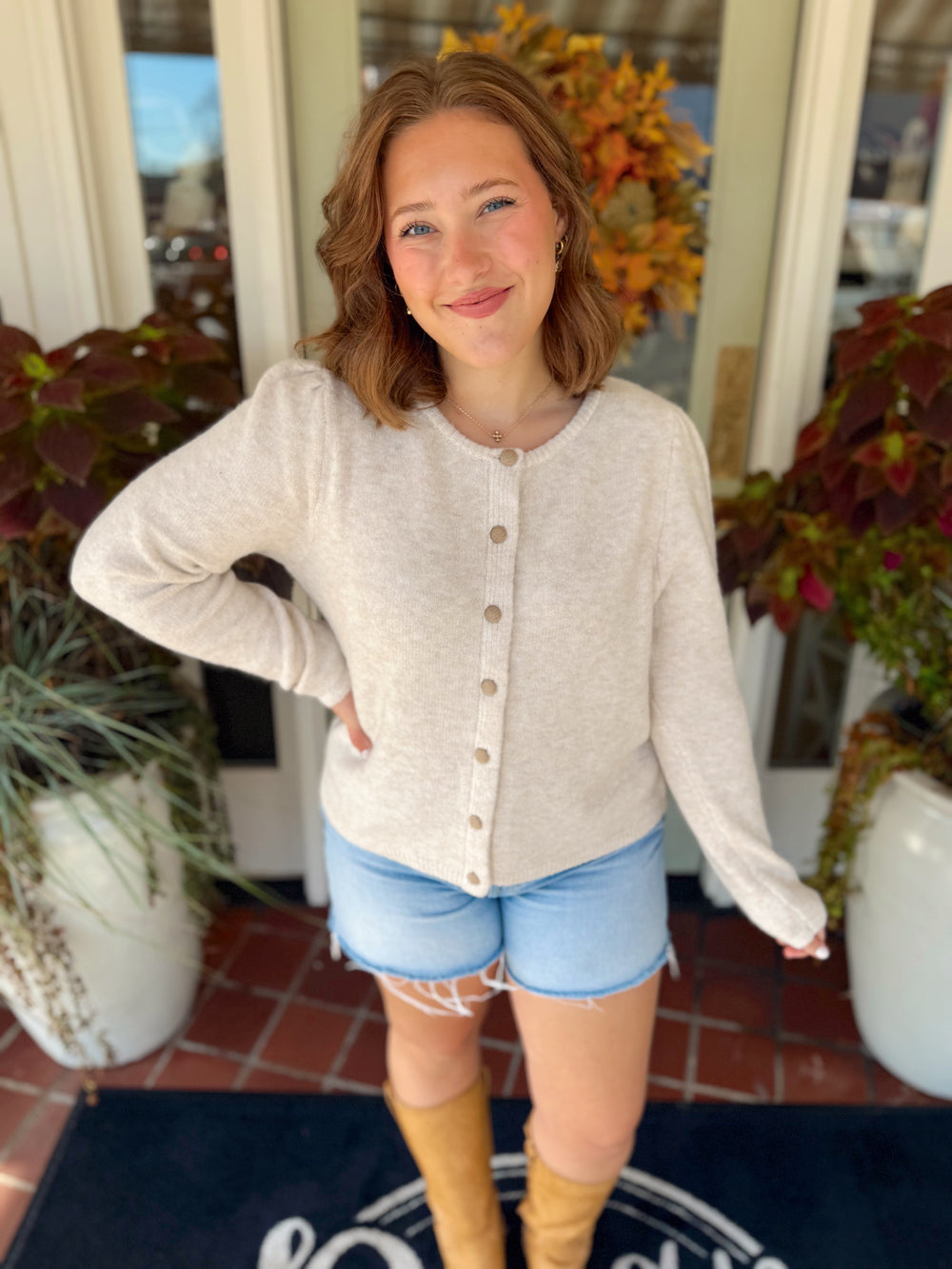 This soft cream cardigan features a simple round neckline, subtle gathered shoulders, and tonal textured buttons down the front.