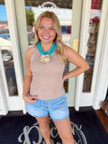 Woman wearing a taupe ribbed sleeveless knit tank top paired with light wash denim shorts and a turquoise statement necklace.
