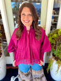 This vibrant magenta lace blouse features a flowy, relaxed silhouette with a gathered neckline and delicate tie detail.