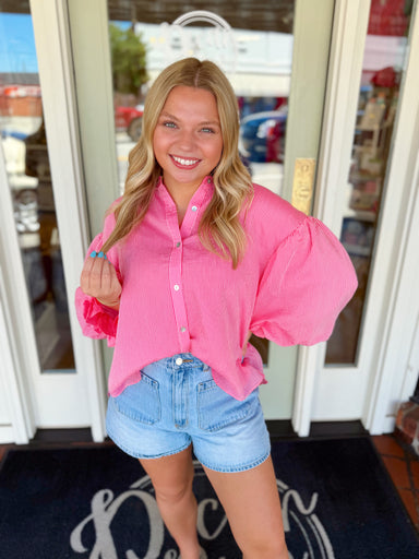 Woman wearing a pink striped button-down blouse with statement puff sleeves paired with light wash denim shorts.
