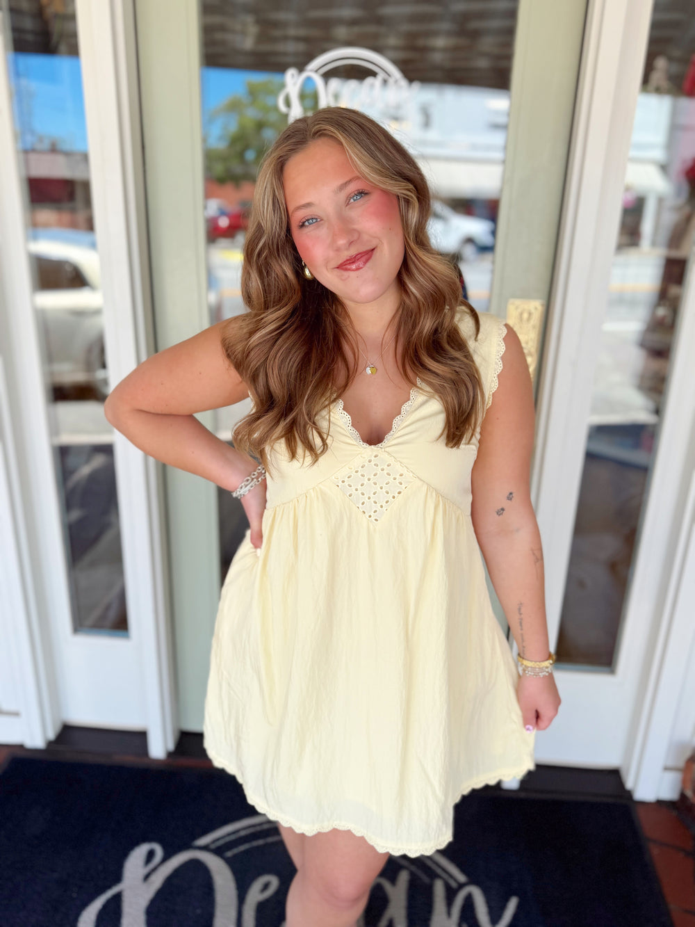 Woman wearing a soft yellow babydoll mini dress with lace trim neckline, eyelet bodice detail, and flowy silhouette.
