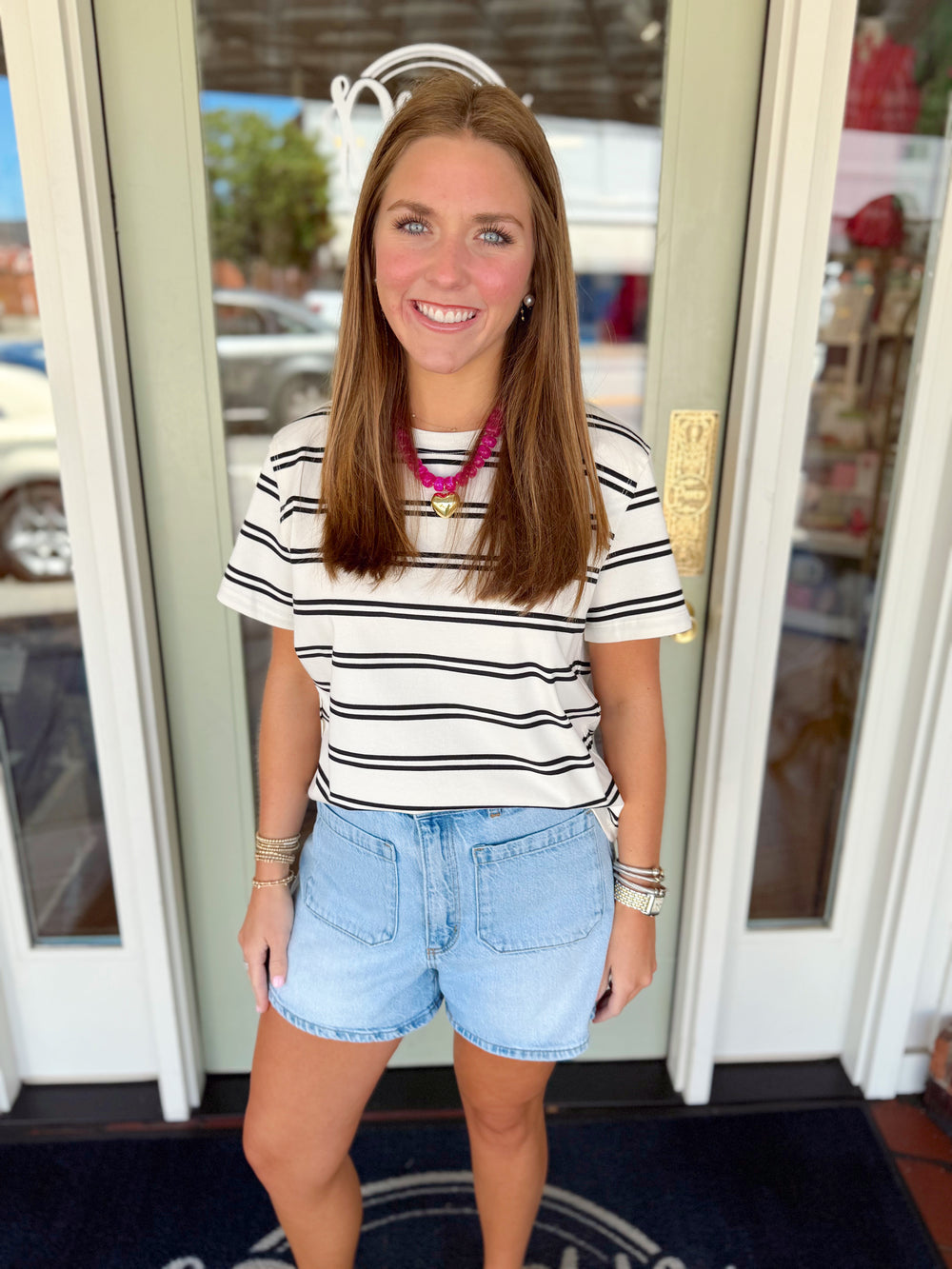 Woman wearing an ivory short sleeve striped tee with black stripes paired with light wash denim shorts.
