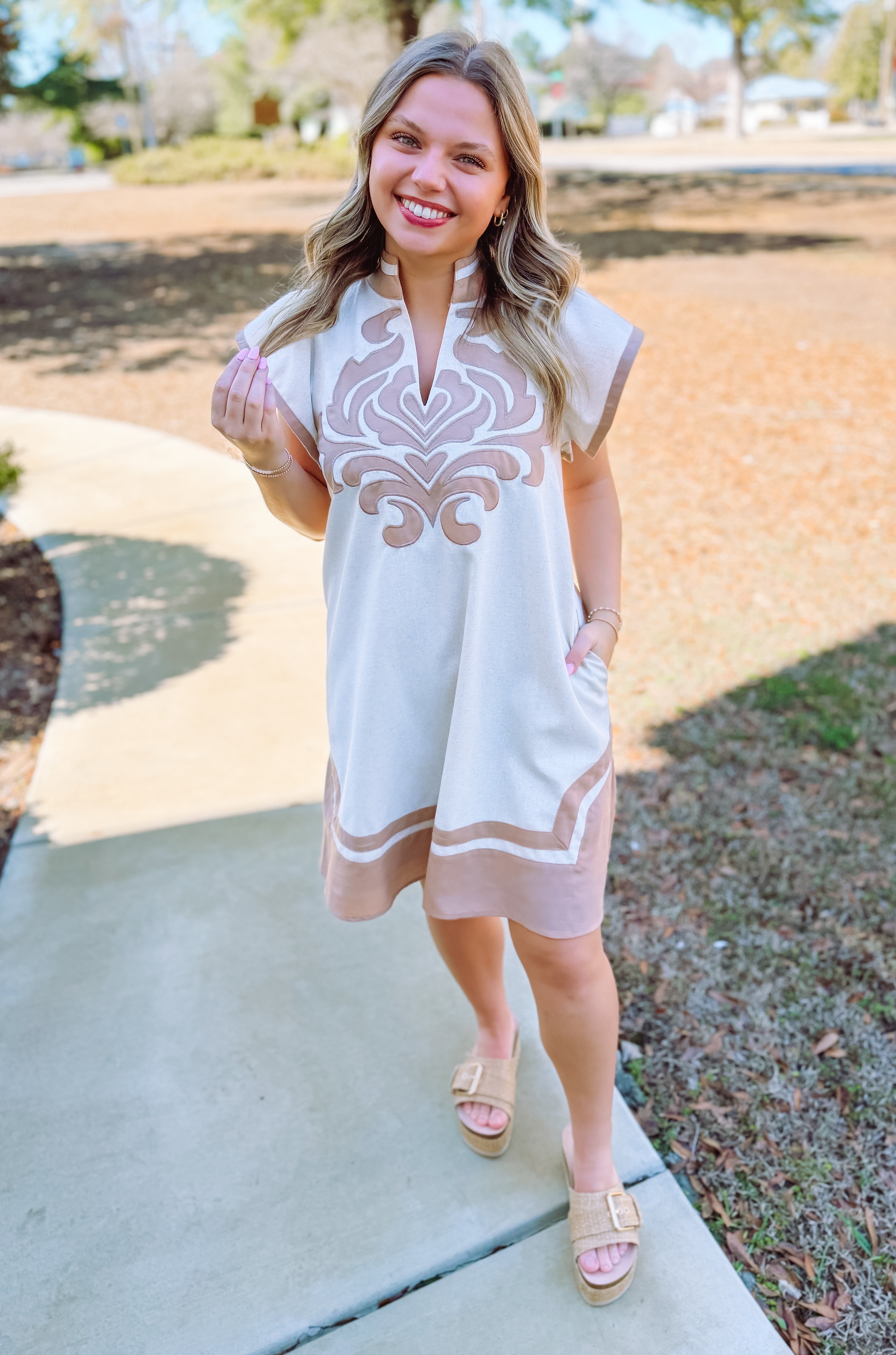 Neutral linen mini dress with pockets and embroidered applique. 