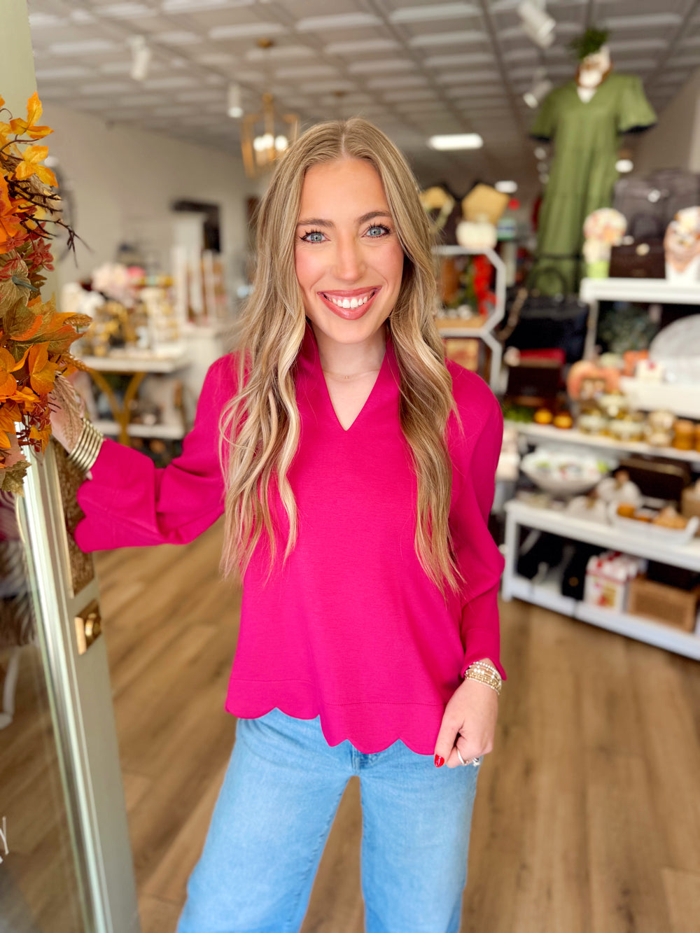  This vibrant fuchsia top features a structured split neckline, softly gathered shoulders, and scalloped trim along the hem and sleeve cuffs