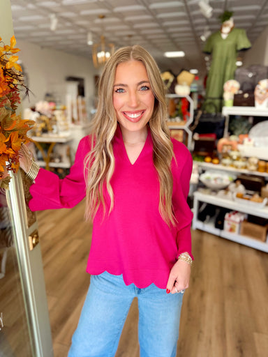  This vibrant fuchsia top features a structured split neckline, softly gathered shoulders, and scalloped trim along the hem and sleeve cuffs