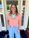 Woman wearing a blush pink short sleeve tee with rolled sleeves paired with light wash denim jeans and a colorful floral neck scarf.