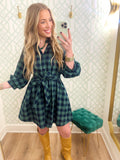 This dress features a rich green and navy buffalo plaid with a button-front design and a removable self-tie belt to define the waist.