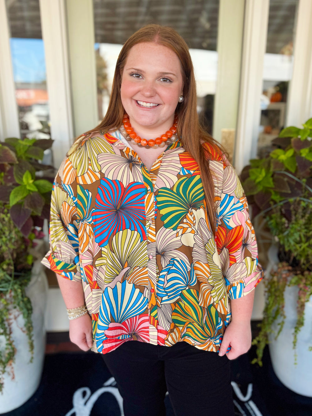  This tropical leaf print top features a vibrant mix of colors with a classic collared neckline and button-down front. 