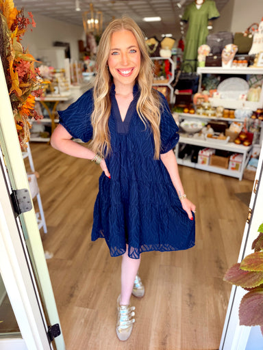  This navy mini dress features a subtle textured pattern throughout with a relaxed tiered silhouette that gives it plenty of movement. 