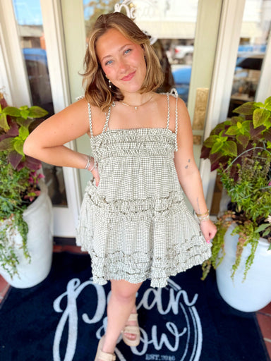 This mini dress features a classic gingham print with pretty ruffle detailing along the top and a flowy tiered silhouette.