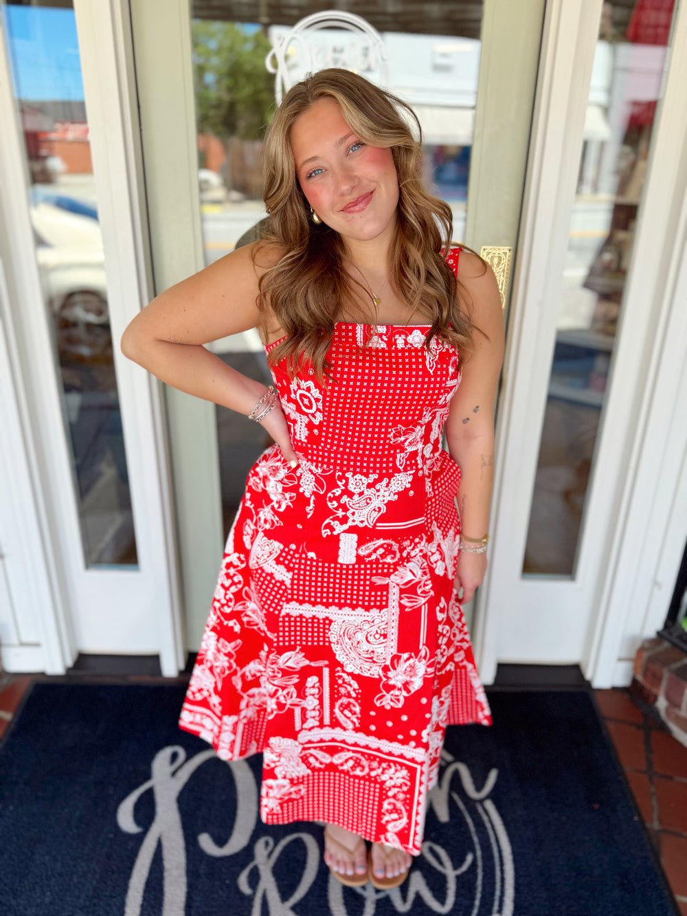 Woman wearing a red and white patchwork print midi dress with floral and gingham patterns, fitted bodice, and flowy skirt.