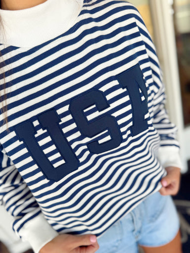 Woman wearing a navy and white striped USA pullover sweatshirt paired with light wash denim shorts.

