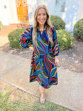  This dress features a colorful abstract botanical print with rich shades of navy, green, red, purple, and camel. 