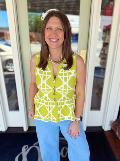 Woman wearing a chartreuse green and white geometric print sleeveless peplum top with gold button details paired with light wash denim jeans and gold jewelry.
