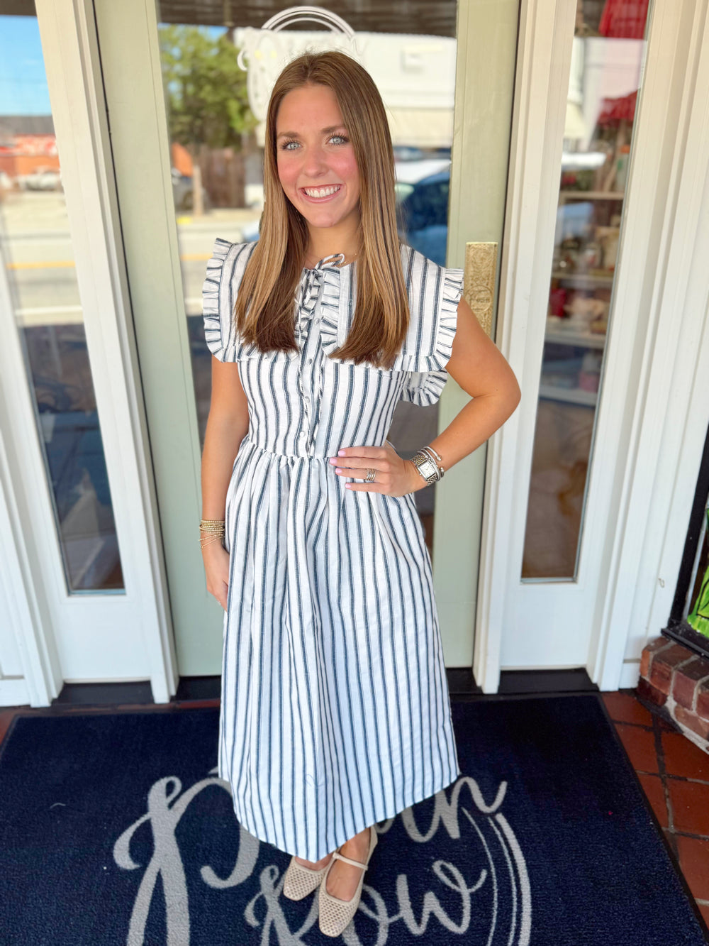 Woman wearing a black and ivory striped midi dress with ruffled cap sleeves, button-front detail, and fitted waist.
