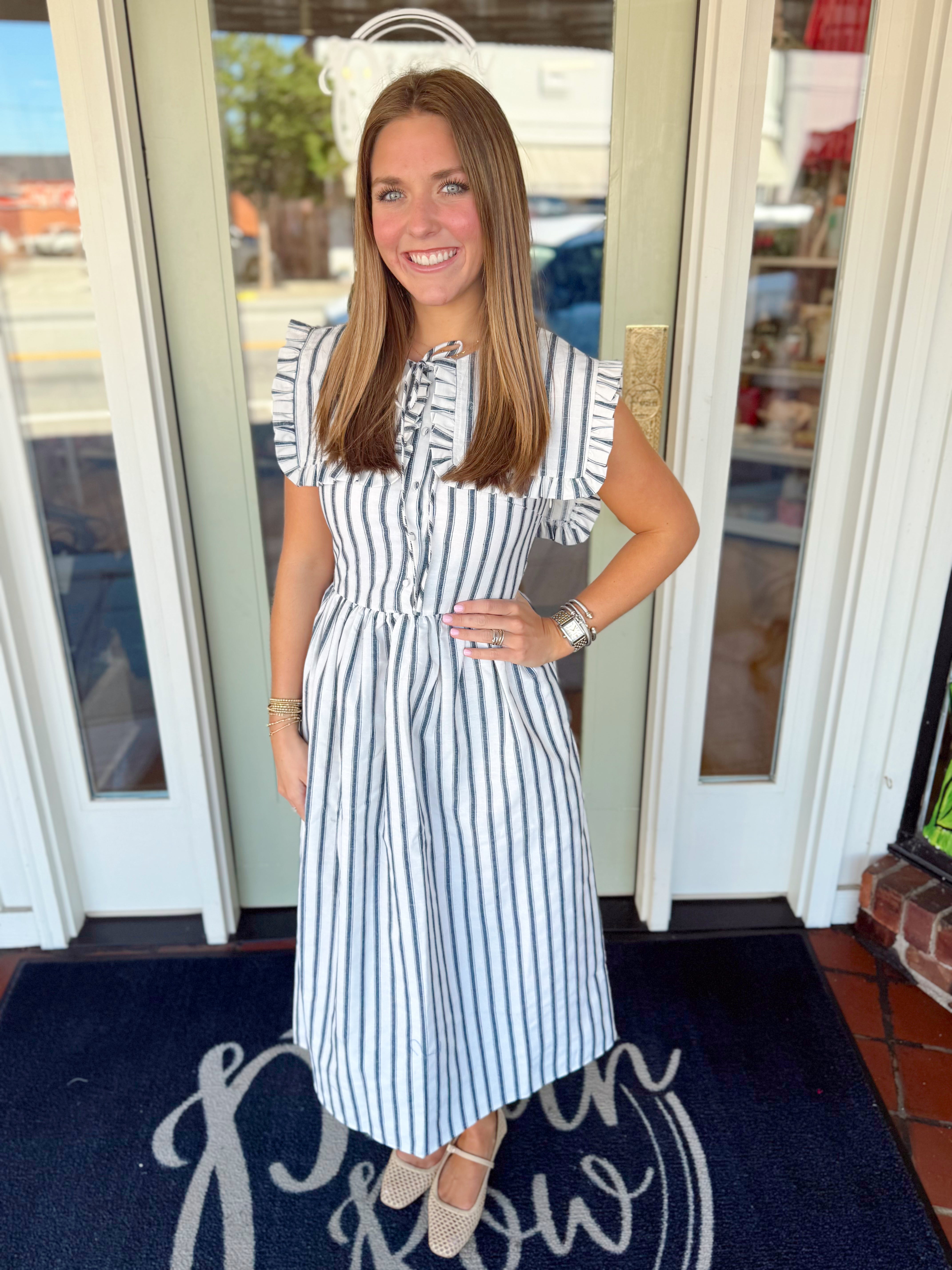 Woman wearing a black and ivory striped midi dress with ruffled cap sleeves, button-front detail, and fitted waist.
