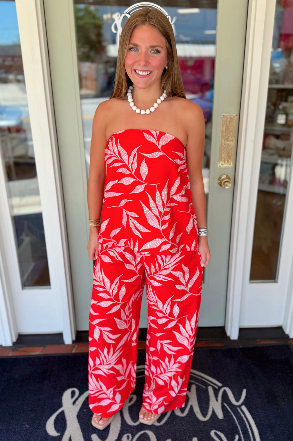 Strapless coral-red top featuring a blush tropical leaf print, elastic neckline, and relaxed flowy silhouette.