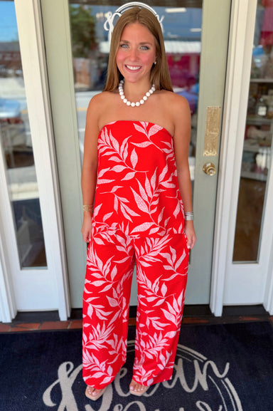 Strapless coral-red top featuring a blush tropical leaf print, elastic neckline, and relaxed flowy silhouette.