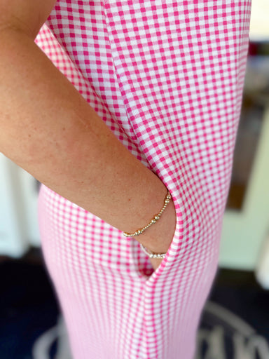 Woman wearing a pink and white gingham mini dress with scalloped flutter sleeves, collared neckline, button detail, and side pockets.