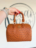This rich cognac handbag features an ostrich-inspired textured finish, structured barrel silhouette, and coordinating top handles.