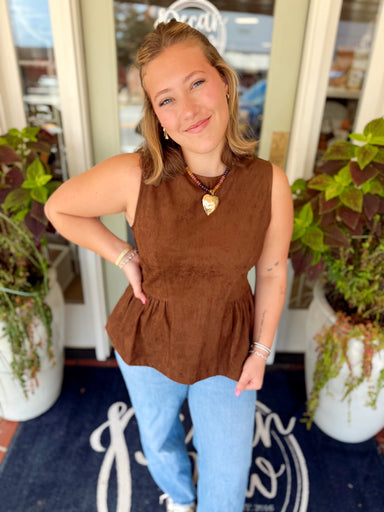 This rich chocolate brown sleeveless top features a soft suede-inspired finish with a fitted bodice that flows into a feminine peplum hem.