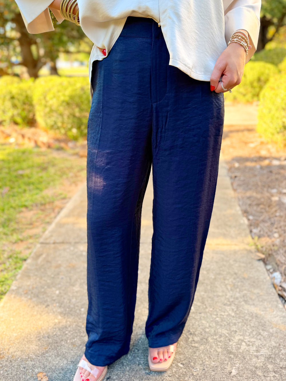 These pants feature a sleek navy finish with a subtle satin sheen, a flattering high-rise waist, and a relaxed straight-leg silhouette.