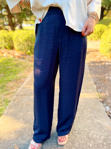 These pants feature a sleek navy finish with a subtle satin sheen, a flattering high-rise waist, and a relaxed straight-leg silhouette.