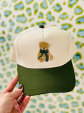 green bill hat with a teddy bear with a green bow around his neck 