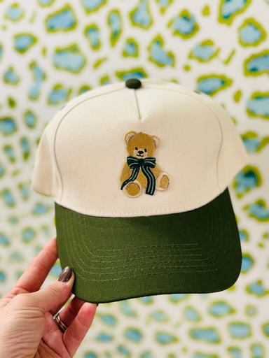 green bill hat with a teddy bear with a green bow around his neck 
