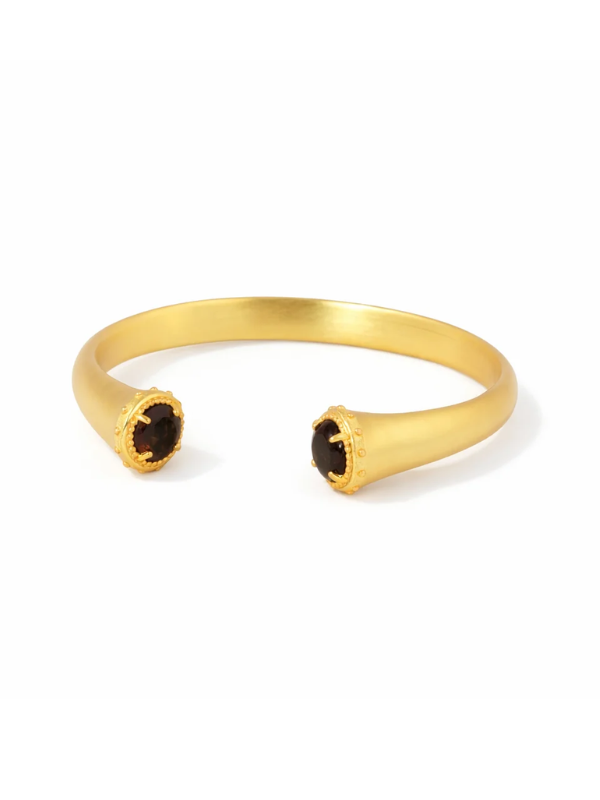 A gold-toned open cuff bracelet with two textured circular dark brown gemstone accents at the ends, shown on a clean white background.