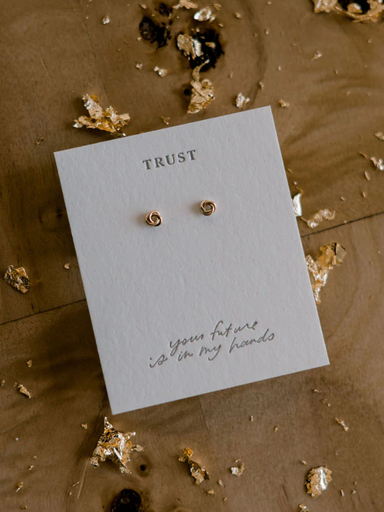 Gold spiral earrings on a card with text on a wooden surface