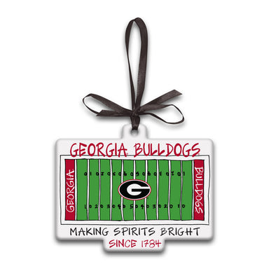 A Georgia Bulldogs ornament shaped like a football field, with a dark brown ribbon loop at the top. The design features a green field, white yard lines, red side banners reading 'GEORGIA' and 'BULLDOGS', a large 'G' logo in the center, and text reading 'GEORGIA BULLDOGS' and 'MAKING SPIRITS BRIGHT SINCE 1784'.
