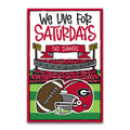 A rectangular printed sign or poster with a red border and the text 'We Live For SATURDAYS' above an illustrated football stadium, crowd, football, and a red helmet with a Georgia 'G' logo.