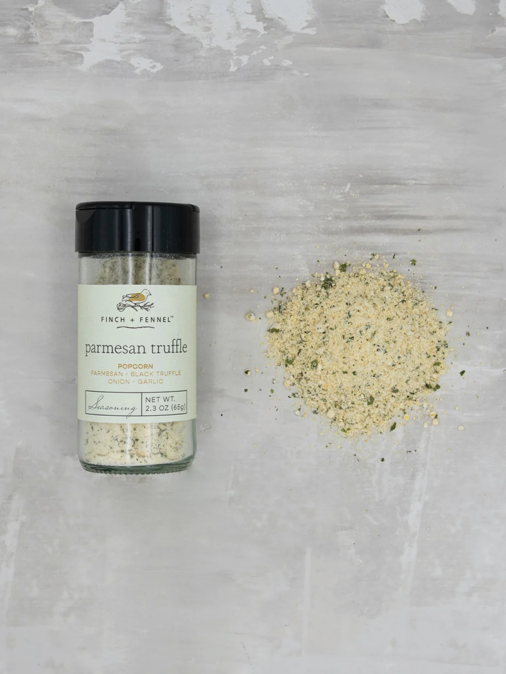 Bottle of Finch + Fennel Parmesan Truffle Popcorn Seasoning beside a mound of savory seasoning blend, featuring parmesan cheese, black truffle, garlic, and onion for gourmet popcorn flavor.