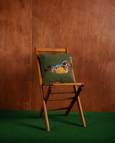 Wooden chair with a green cushion featuring a duck design against a wooden wall.