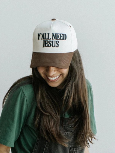 A woman is wearing a white embroidered hat with the text 'Y'ALL NEED JESUS' on the front.