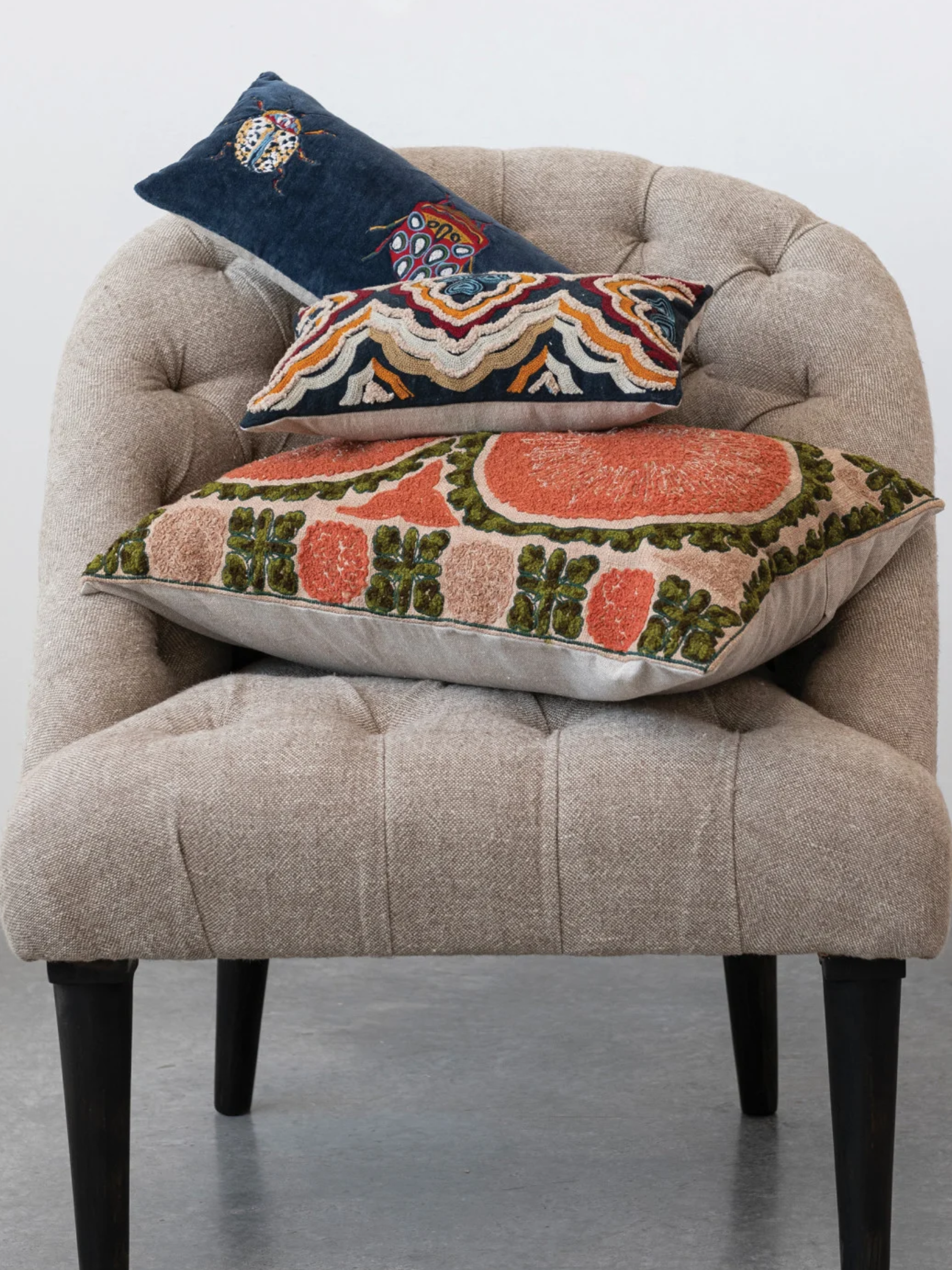 Navy velvet lumbar pillow with three colorful embroidered beetles across the front in a chair with other pillows