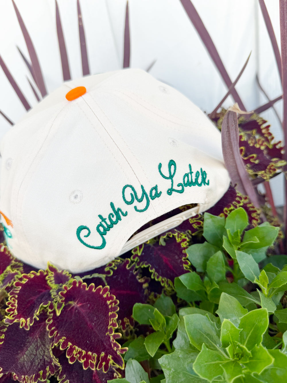 Cream trucker hat with embroidered “Gone Fishin’” lettering, aqua striped brim, fishing lure embroidery on the side, and “Catch Ya Later” embroidered on the back.
