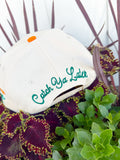 Cream trucker hat with embroidered “Gone Fishin’” lettering, aqua striped brim, fishing lure embroidery on the side, and “Catch Ya Later” embroidered on the back.
