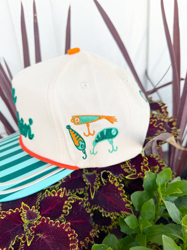 Cream trucker hat with embroidered “Gone Fishin’” lettering, aqua striped brim, fishing lure embroidery on the side, and “Catch Ya Later” embroidered on the back.
