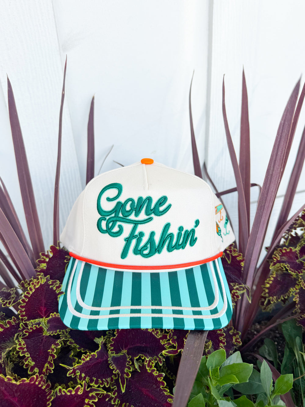 Cream trucker hat with embroidered “Gone Fishin’” lettering, aqua striped brim, fishing lure embroidery on the side, and “Catch Ya Later” embroidered on the back.
