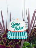 Cream trucker hat with embroidered “Gone Fishin’” lettering, aqua striped brim, fishing lure embroidery on the side, and “Catch Ya Later” embroidered on the back.
