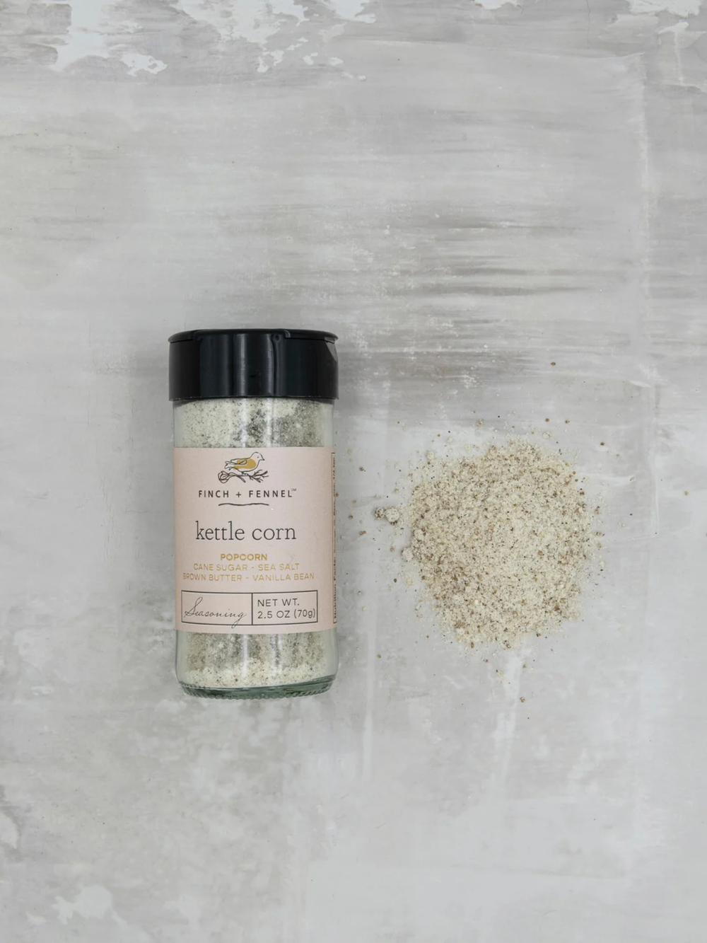 Bottle of Finch + Fennel Kettle Corn Seasoning beside a pile of seasoning blend, featuring cane sugar, sea salt, brown butter, and vanilla bean for sweet-and-salty gourmet popcorn.